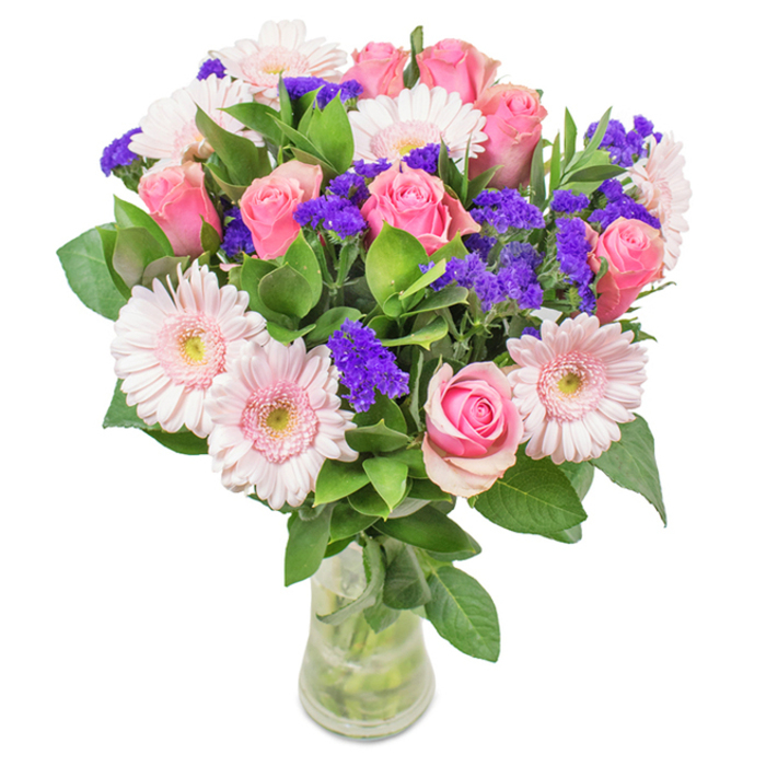 A stunning display by Beddington Florist, this hand-arranged floral bouquet features approximately seven to nine softly blushed and mid-pink roses, their petals tightly furled or just beginning to open, forming elegant spirals. Surrounding them, five to seven pale pink Gerbera daisies bring an airy touch, with their large, round faces and gently radiating petals fading to creamy white centers. Interwoven among these main blooms, vivid clusters of purple statice-recognized by their papery texture and deep tone-offer striking contrast and a lively element of surprise. Generous deep green foliage, glossy and abundant, acts as a verdant base, recalling the lush hedgerows of central Beddington. Arranged in a crystal-clear glass vase, where stems and water are visible through the polished surface, this bouquet suggests freshness as if picked from a well-tended local garden. It's perfect for birthdays, anniversaries, or as a sophisticated decorative touch in a Beddington home or office, conveying a message of joy, celebration, and heartfelt connection to the community.