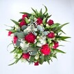 From a high, top-down view, this generous bouquet appears as a perfectly rounded tapestry of colour, texture, and movement, set against a clean white background that lets every bloom shine. At its centre, velvety crimson red roses in varying stages of opening create a rich, romantic core; some are still tightly furled, while others begin to spiral open, revealing layers of soft, luxurious petals. Nestled beside them are ruffled fuchsia and ruby red carnations, their frilled edges catching the light and giving the arrangement a festive, almost celebratory rhythm, like laughter shared over a family table in Beddington. Threaded between the deeper tones, small clusters of crisp white spray chrysanthemums and other daisy-like blooms add brightness and clarity, their neat petals forming tiny halos of light. The bouquet is dusted with countless tiny white gypsophila florets, or baby's breath, which float between the larger flowers like a soft, misty veil, softening every transition. Around and beneath these blooms, lush greenery provides structure and contrast: strong, pointed dark green leaves, likely lily or alstroemeria foliage, fan outward to create a solid frame, while silvery-green, rounded eucalyptus leaves weave through with a cooler, contemporary note and a hint of fresh woodland scent. The result feels abundant yet balanced, as if freshly arranged on a florist's bench just off a quiet Beddington side street, perfect for marking an anniversary, sending a heartfelt get well wish, or simply surprising someone at home with a vivid burst of love and vitality.